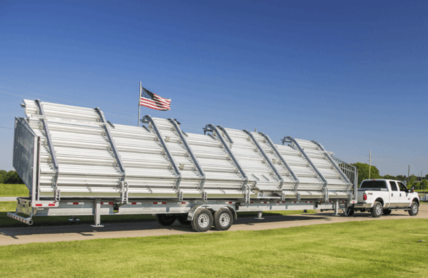 Hydraulic portable aluminum bleachers folded and secured on trailer being towed by pickup truck across grass field.